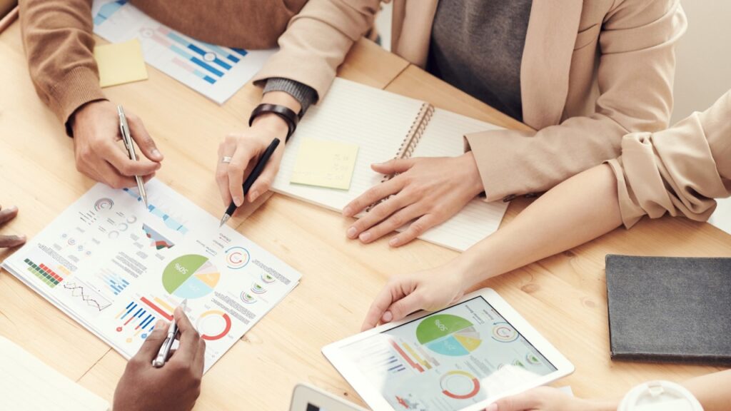 Group of professionals analyzing digital marketing reports and business performance charts on paper and tablet during a strategy meeting. This image reflects practical learning, teamwork, and data-driven decision-making as taught at HIDM – Hisar Institute of Digital Marketing.