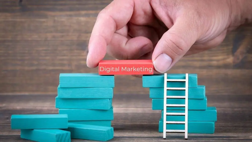 A hand placing a red block labeled "Digital Marketing" between two stacks of blue blocks with a ladder—symbolizing the strong foundation provided by HIDM in digital marketing fundamentals, including SEO basics, content strategy, website structure, and social media setup.