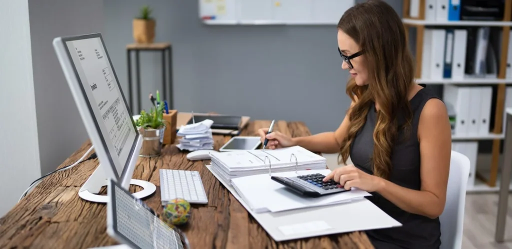 A professional woman working at a desk with a computer, calculator, and documents—illustrating HIDM’s focus on analytics and freelancing opportunities, including training in Google Analytics, performance tracking, client reporting, and building a successful freelance digital marketing career.