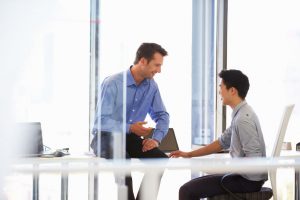 Two business professionals having a friendly discussion in a modern office setting, representing mentorship and communication skills, connected to Er. Manmohan Singlaa’s corporate training expertise.