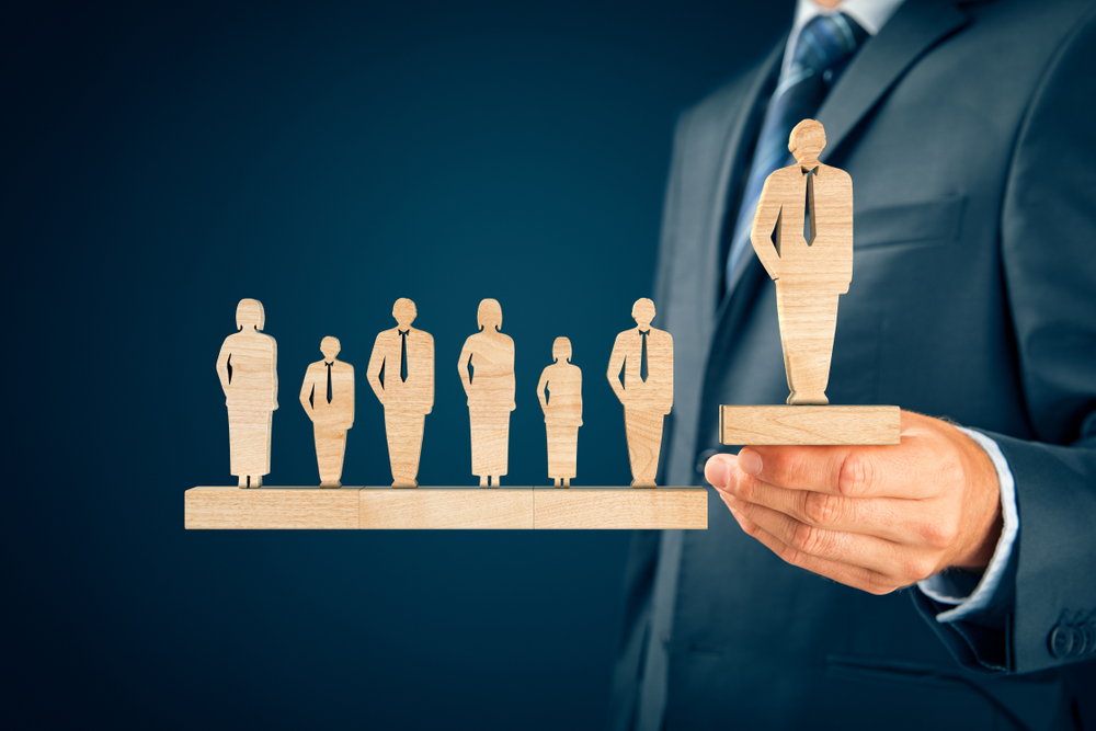 Business concept showing wooden human figures representing a team, with one figure elevated as a leader, symbolizing leadership and team management, related to Er. Manmohan Singlaa’s leadership development expertise.