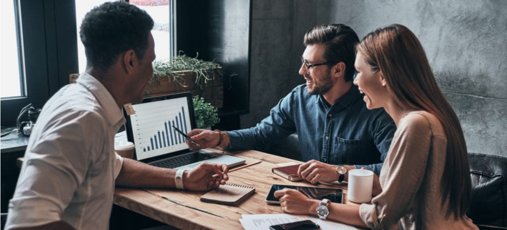 "Affiliate marketers discussing business growth strategies with HiDM Digital Marketing insights, analyzing sales performance charts on a laptop in a collaborative meeting environment."