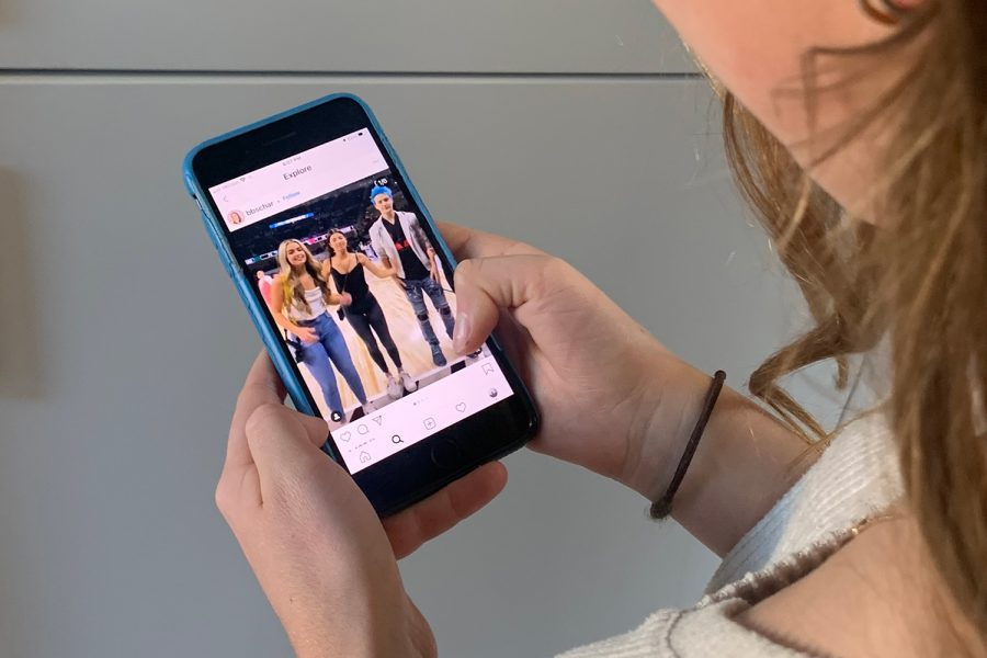 Close-up of a person holding a smartphone and scrolling through an Instagram video featuring a group of young people, representing the HiDM digital marketing mistake of posting randomly on social media without a content strategy.