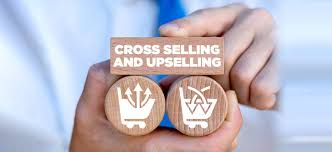 "Close-up of a person holding wooden blocks with shopping cart icons, one representing upselling and the other cross-selling, with a block on top labeled 'Cross Selling and Upselling'."