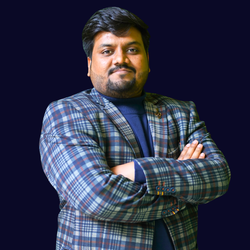 A portrait of a smiling man with a beard, wearing a plaid blazer over a navy blue turtleneck with arms crossed against a dark background.