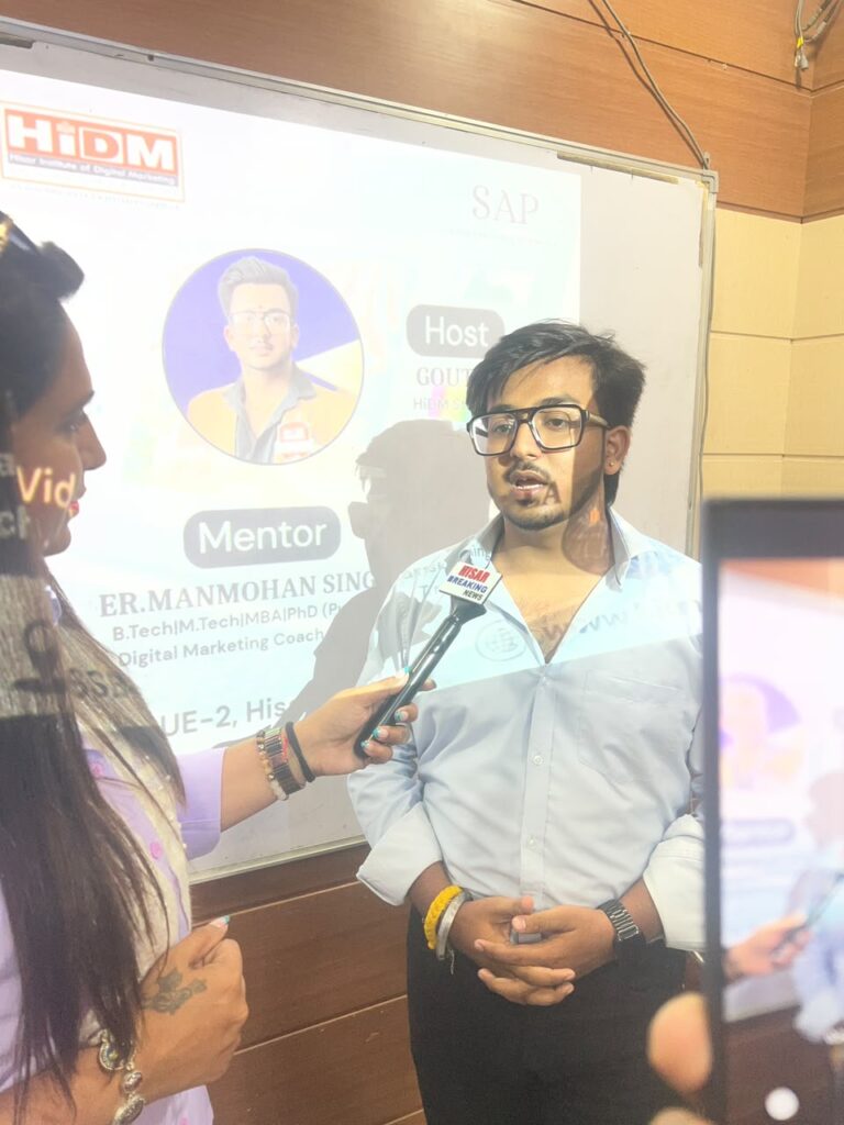Goutam giving a live media interview during the VN AI Editor seminar at HiDM while speaking into a news microphone. The seminar presentation is displayed on the projector screen in the background as a reporter records the interaction.