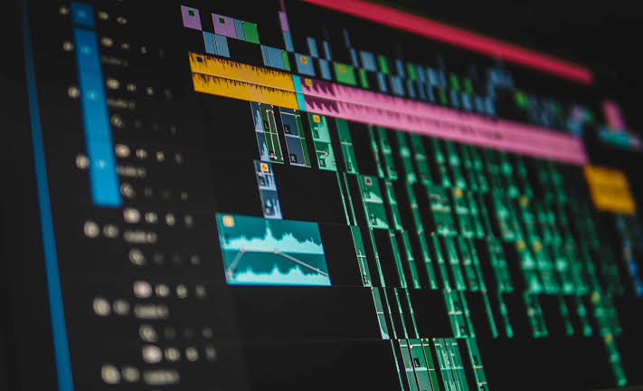 Close-up view of a professional video editing timeline displayed on a computer monitor, showing multiple video clips, audio tracks, transitions, and color-coded editing layers used for post-production and digital content creation.