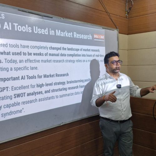 Ishaan, an HIDM student, delivering a seminar presentation on AI tools used in market research while standing beside a projected slide titled “Top AI Tools Used in Market Research.”